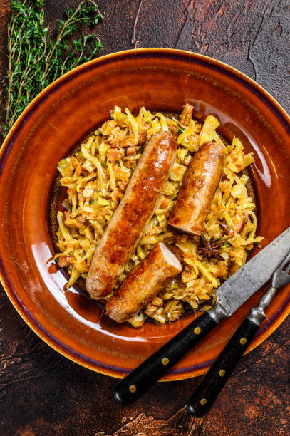 repollo guisado bigos con champiñones y salchichas de carne en un plato. fondo oscuro. vista superior - bigos fotografías e imágenes de stock