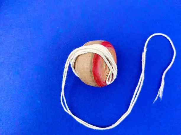 Top view of wooden spinning top with a white rope on blue background