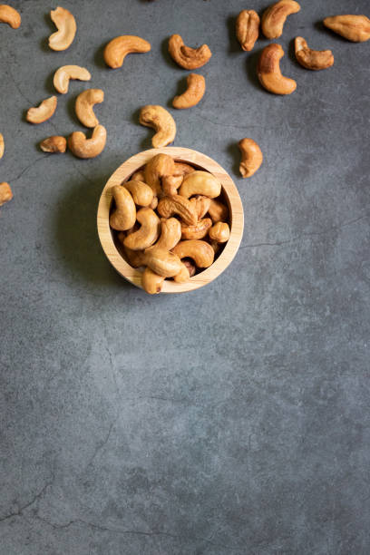 istock Cashew nuts in wooden bowl on dark table background with copy space, top view. 1303695230