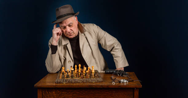 istock Senior male chess player at a table alone, dressed in beige overcoat and hat, copy space provided 1303698348