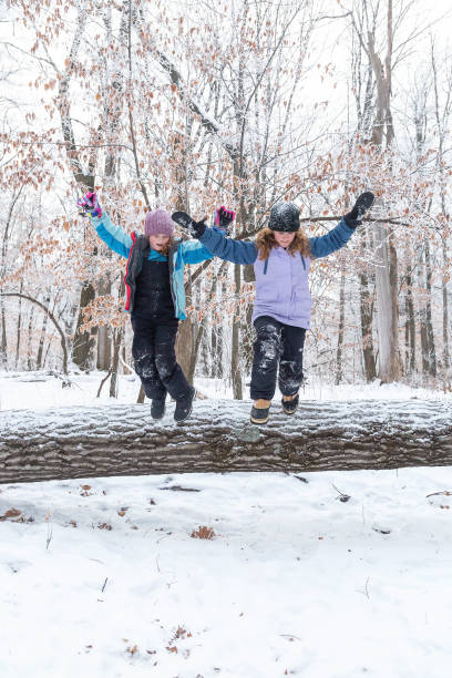 istock Girls Jumping Off Fallen Tree in Winter Woods 1303700888