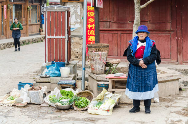 Naxi woman selling vegetables in the streets of Baisha village Baisha, China - January 14, 2018: Naxi woman selling vegetables in the streets of Baisha village, Yunnan, China yunnan province stock pictures, royalty-free photos & images