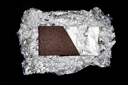 Sweet and delicious chocolate bar on silver foil on black background photo taken from above