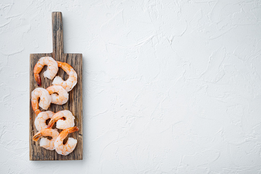 Whole fresh peeled cooked prawns, shrimps set, on wooden cutting board, on white background, top view flat lay , with copyspace  and space for text