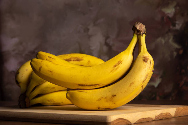 istock Bananas put on wood on a table, dark abstract background, directional light, selective focus. 1303703275