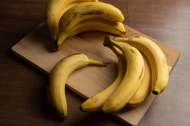 istock Bananas put on wood on a table, dark abstract background, directional light, selective focus. 1303703284