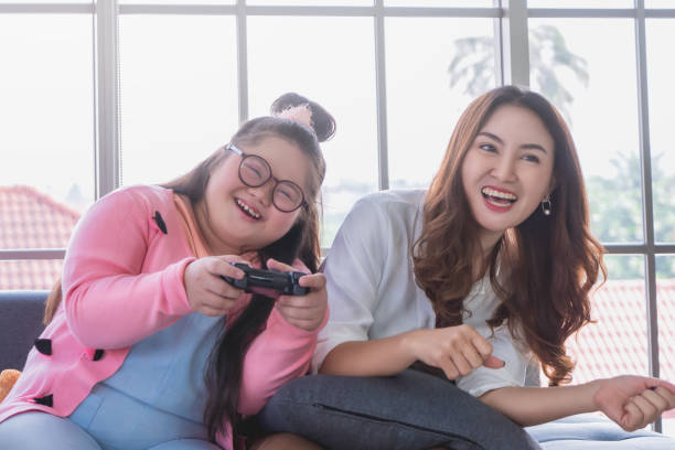 어머니와 함께 하는 오스트리즘 차일드는 다운 증후군 가족 양성 개념에 대한 미소와 행복으로 집에서 비디오 게임을 함께 하고 있습니다. - video game family child playful 뉴스 사진 이미지