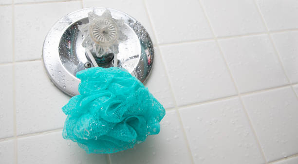 una esponja loofah azul colgando en una ducha húmeda en el medidor de temperatura. - esponja de lufa fotografías e imágenes de stock