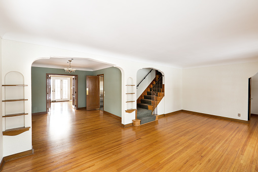 A 1930s American Tudor Revival Style Real Estate Interior Living Room and dining in the mid-west of United States for sale. The empty vacant property featuring built-in woodwork shelving, double French doors and staircase to second floor, oak hardwood flooring.