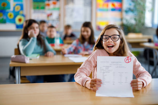 Happy schoolgirl showing her A grade on a test at elementary school Happy schoolgirl showing her A grade on a test at elementary school good grades stock pictures, royalty-free photos & images