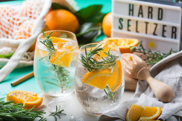 Hard seltzer cocktail with orange and zero waste bartenders accessories Hard seltzer cocktail with orange, rosemary and ice on a table. Summer refreshing beverage, drink with trendy zero waste accessories, bamboo straw and mesh bag. tonic water stock pictures, royalty-free photos & images