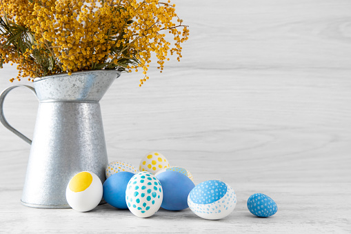Easter eggs and bouquet of flowers in front of gray wooden wall and table with copy space