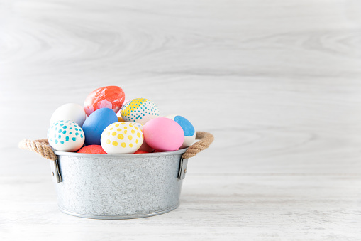Easter eggs painted in pastel colors in a basket on white wooden background.