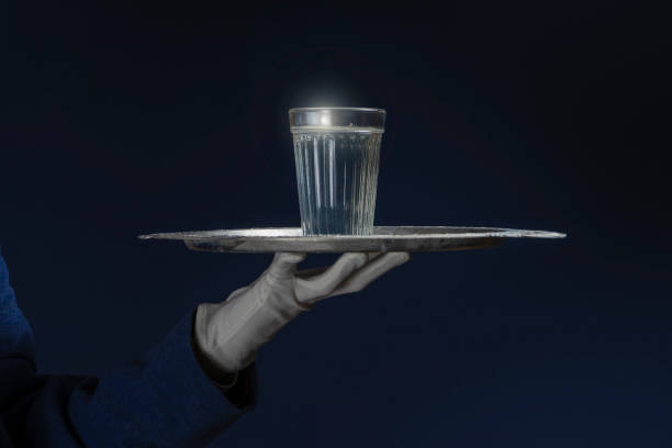 un mayordomo con guante blanco sostiene una bandeja en la que se encuentra un vaso de agua. fondo negro. - waiter butler champagne tray fotografías e imágenes de stock