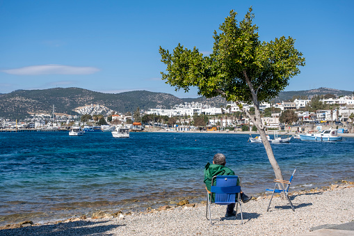 In spring time, a seascape view; sailboats, pier and city view of Bodrum (Halicarnassus). Old man sitting in sea side alone.