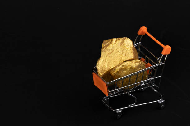 Raw gold piece on a miniature shopping cart. Shiny raw gold bullion on a miniature shopping cart with black background and copy space. wholesale direct metals gold ira stock pictures, royalty-free photos & images