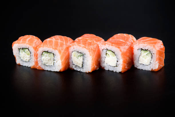 sushi roll cibo di mare su sfondo nero. consegna di sushi dal ristorante. delizioso sushi giapponese fresco con avocado, cetriolo, gamberetti e caviale su sfondo scuro - fruit table bamboo black foto e immagini stock
