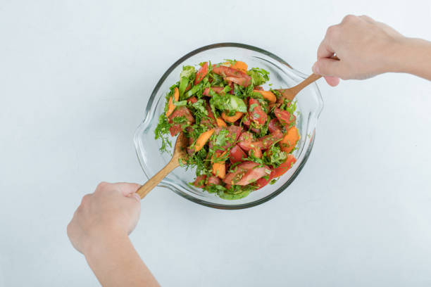 istock Hands mixing delicious vegetable salad on a glass plate 1303722064