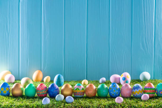 istock Easter eggs on turf grass and blue wooden wall with spring flowers 1303722238