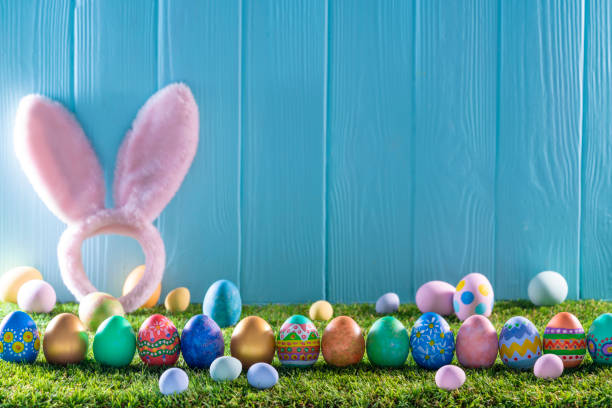 istock Easter eggs on turf grass and blue wooden wall with spring flowers 1303722263