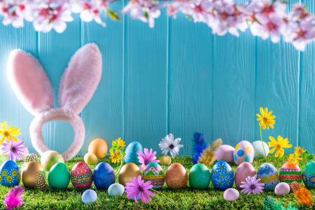 istock Easter eggs on turf grass and blue wooden wall with spring flowers 1303722783