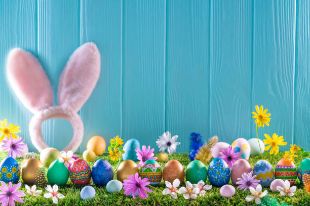 istock Easter eggs on turf grass and blue wooden wall with spring flowers 1303722810