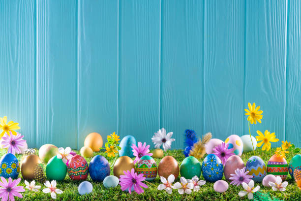 istock Easter eggs on turf grass and blue wooden wall with spring flowers 1303722839