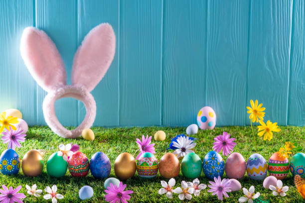 istock Easter eggs on turf grass and blue wooden wall with spring flowers 1303722933