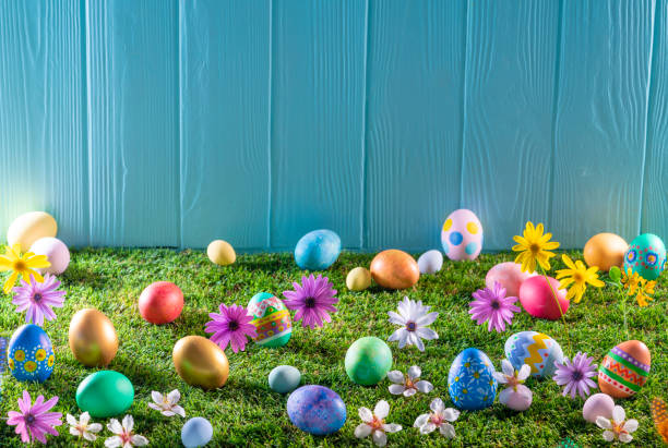 istock Easter eggs on turf grass and blue wooden wall with spring flowers 1303723124