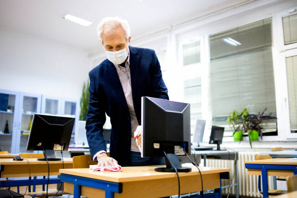 istock Professor prepares the classroom between classes by taking care of all contact surfaces with disinfectant stock photo 1303729258