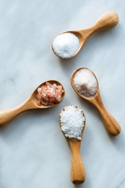 Salt Types Various salt types in 4 wooden spoons on white marble. bath salt stock pictures, royalty-free photos & images