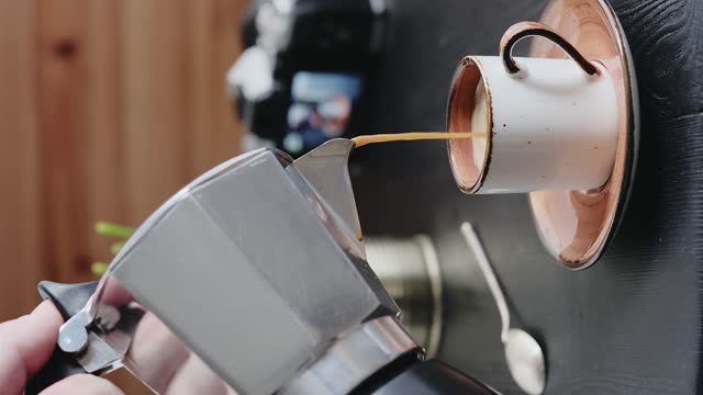 Breakfast in a cafe, espresso is poured from a geyser coffee maker (moka pot) into a cup, close-up, selective focus. Steam rises above the cup of freshly brewed coffee