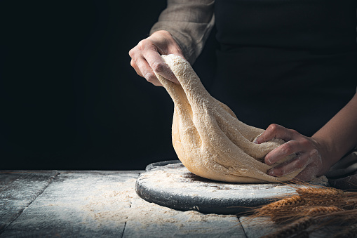 Dough in the hands of a woman cook on a wooden background with flour and wheat ears. Cooking concept.
