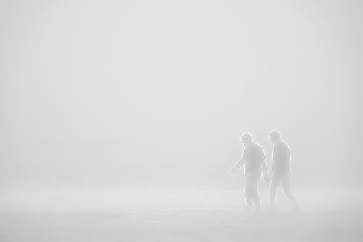 Man and woman walking together in shallows along a beach on a foggy morning on the Gulf Coast of west central Florida, with digital painting effect in black and white