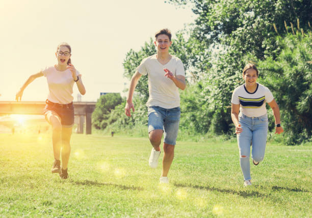 wesołe nastolatki biegają razem w letnim parku miejskim - teenagers only lake summer sunlight zdjęcia i obrazy z banku zdjęć