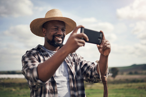 Shot of a mature man using a smartphone to take pictures of a farm