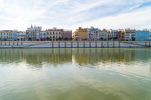 Front view of the famous Betis street of the Triana neighborhood in Seville on a sunny day (Andalusia, Spain). Nice colored houses facing the Guadalquivir river. Emblematic place of the city.