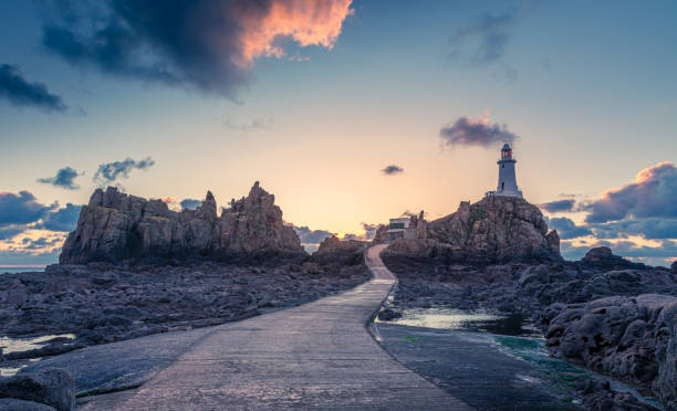 road to la corbiere lighthouse on the sea bottom in a low tide with cliff and sunset,  bailiwick of jersey, channel islands - jersey uk nature landscape imagens e fotografias de stock