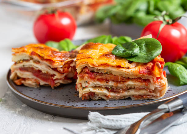 lasagne italienne à la sauce tomate et fromage servi avec tomates et épinards, fond en béton léger. lasagnes végétariennes maison. - repas servi photos et images de collection