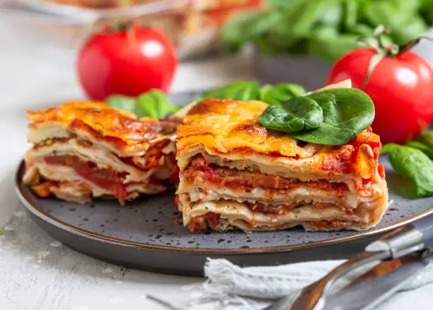 Italian lasagna with tomato sauce and cheese served with tomatoes and spinach, light concrete background. Homemade vegetarian lasagna. Selective focus.