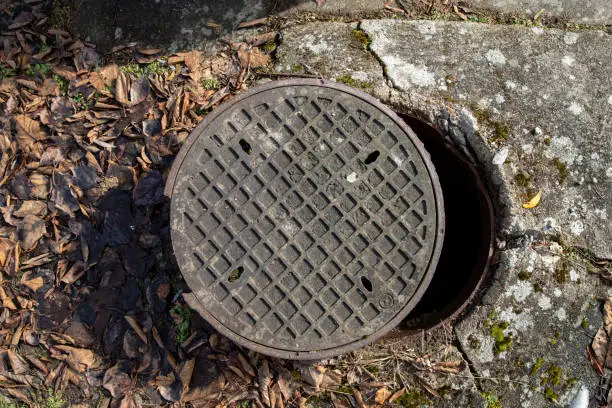 Photo of Open cast iron cover of the sewage chamber. Dangerous glitch for pedestrians on a sidewalk in the city. Spring season.