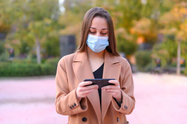 istock woman with mask and mobile phone 1303745812