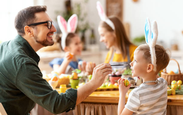 istock Playful father painting sons nose while coloring Easter eggs together 1303747204