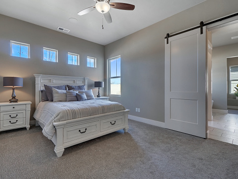 Modern Master Bedroom with new furniture and sliding barn door leading to master bathroom with windows above bed