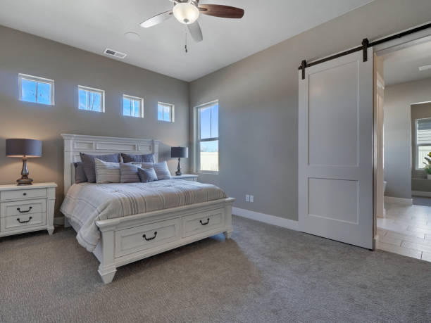 Modern Master Bedroom Staged With New White Furniture Modern Master Bedroom with new furniture and sliding barn door leading to master bathroom with windows above bed owners bedroom stock pictures, royalty-free photos & images