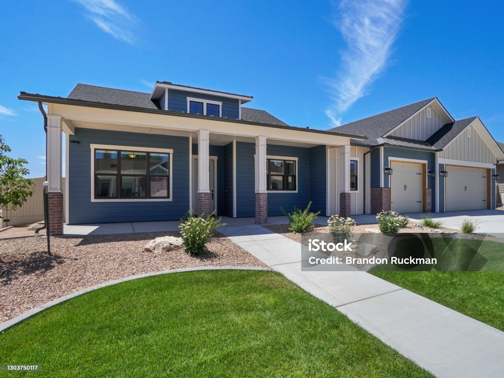 Modern Real Estate Front Exterior Blue and White Color Scheme with landscaping modern landscaped new construction home with blue sky and puffy white clouds. Covered front porch with three car garage Residential Building Stock Photo
