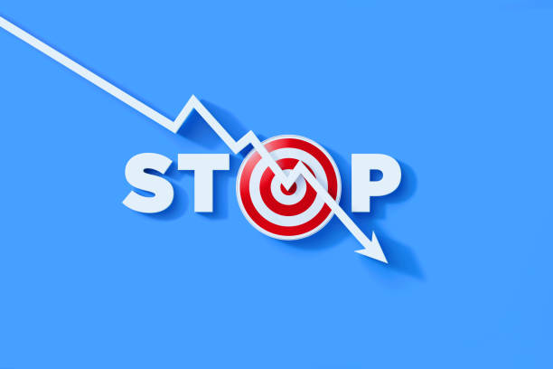 White line graph with arrowhead falling down over stop text and red bull's eye target on blue background. Horizontal composition with copy space. Crisis and loss concept.