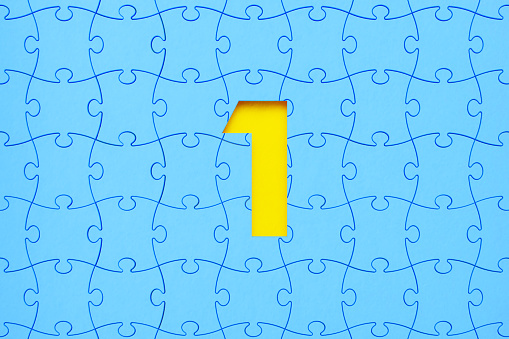 Blue jigsaw puzzle pieces forming a cut out number one on yellow background. Horizontal composition with copy space. Solution concept.