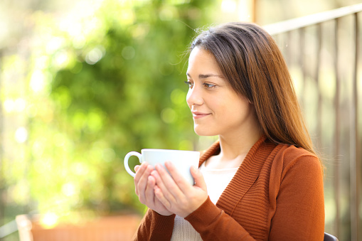 Woman drinking coffee looking away in a garden at home