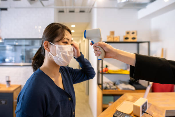 istock Japanese woman measuring temperature using infrared thermometer before entering cafe 1303753988